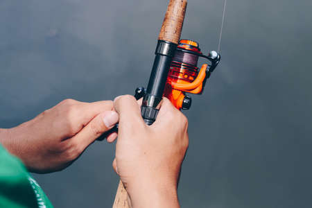 Close up of spinning with the fishing reel in the hand, fishing hook on the line with the bait in the left hand against the background of the water.の写真素材