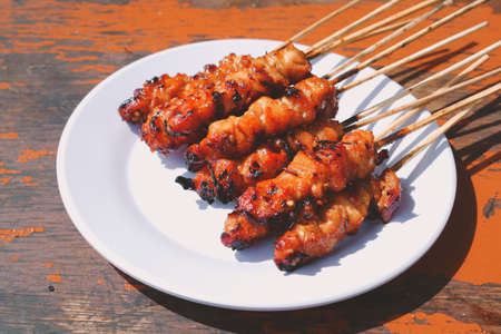 Chicken Satay or Chicken skin satay with red spices on white plate isolated on wooden tables