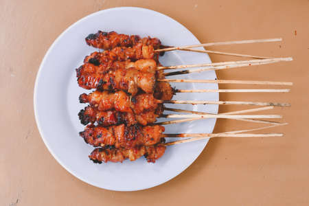Chicken Satay or Chicken skin satay with red spices on white plate isolated on wooden tablesの写真素材