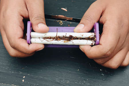 Man hand makes a cigarette with rolling traditional tools, hands closeup.の写真素材