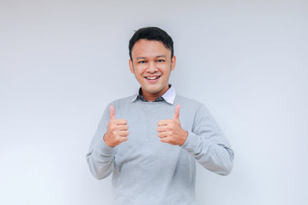 Young Asian man wear grey shirt with happy smiling face and thumbs up or ok sign.の写真素材