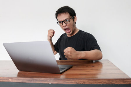 Young Asian man is Angry and hate with laptop. Indonesia Man wear black shirt Isolated grey background.の写真素材