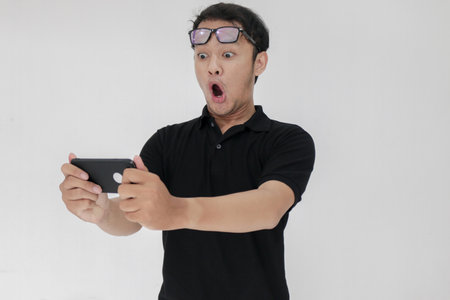 Wow face of Your Asian man shocked what he see in the smartphone on isolated grey background. Indonesia Man wear black shirt Isolated grey background.の写真素材