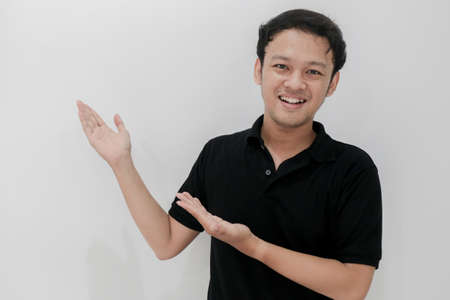 Happy and smile of young Asian man with hand point on empty space. Indonesia Man wear black shirt Isolated grey background.の写真素材