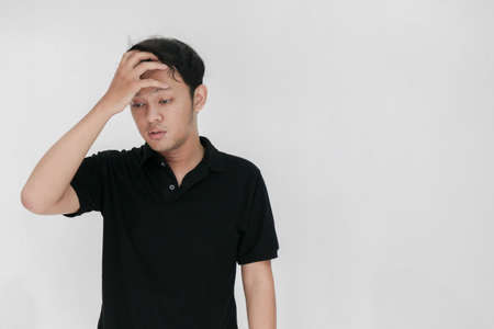 Portrait of young asian man isolated on grey background suffering from severe headache, pressing fingers to temples, closing eyes to relieve pain with helpless face expression.の写真素材