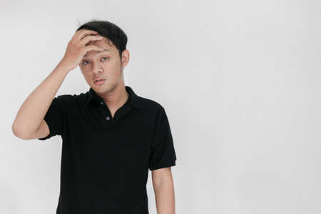 Portrait of young asian man isolated on grey background suffering from severe headache, pressing fingers to temples, closing eyes to relieve pain with helpless face expression.の写真素材