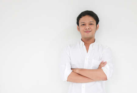 Young Asian man wearing white shirt is holding hands crossed with happy smile and confidence. Successful Indonesian man on gray background.の写真素材