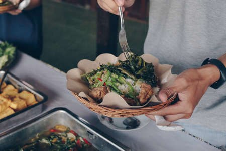 Person hand puts white vegetables from the steel pan to wooden paper plate during lunch in restaurantの写真素材