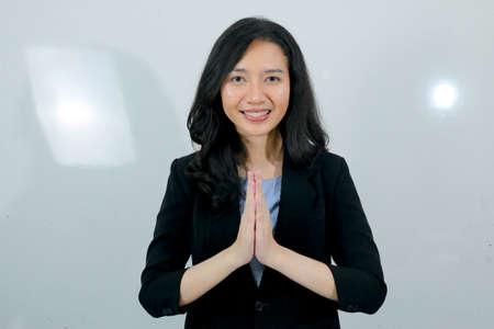 Business young asian girl gives greeting hands at with a big smile on her face. Indonesian woman on gray background.の写真素材
