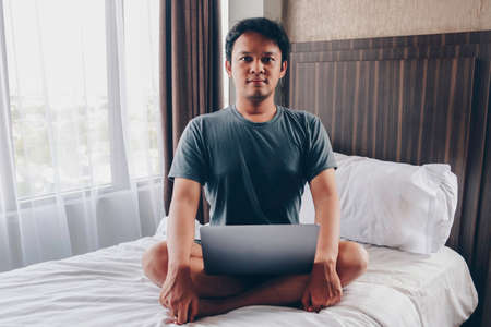 Serious Asian man is working with his laptop on his bed. Concept of freelancer successful lifestyle.の写真素材