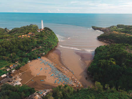 Aerial view of Baron Beach in Gunung Kidul, Indonesia with lighthouse and traditional boat.の写真素材