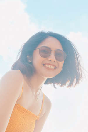 Portrait of happy smiling Asian woman with blue sky view from the bottom.の写真素材