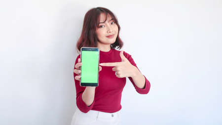 Happy Asian beautiful girl point on green screen phone in white background