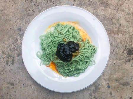 Spice green noodles in white plate with black sauceの写真素材
