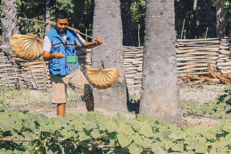 A young asian man in a blue jacket watered plants using a traditional flush tool made of woven palm leavesのeditorial素材