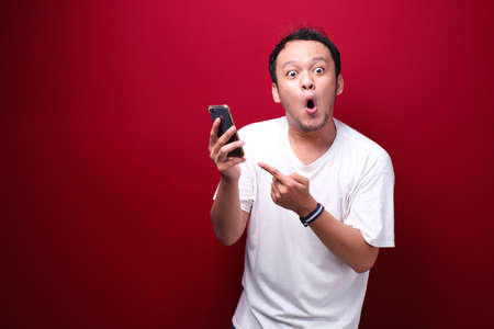 Young asian man shocked when he looking and pointing smartphoneの写真素材