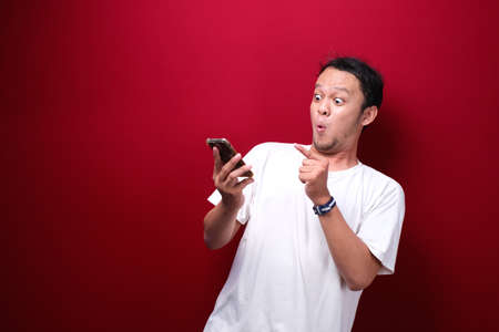 Young asian man shocked when he looking and pointing smartphoneの写真素材