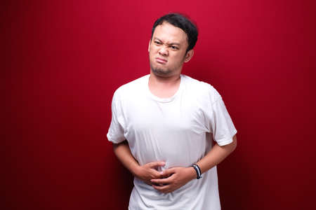 Upset young asian man with serious stomach acheの写真素材