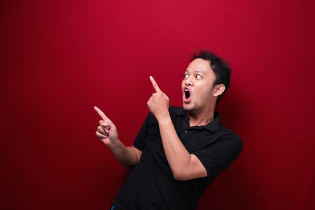 Young asian man is surprised and shouting wow with pointing right with his hand isolated on red background.の写真素材