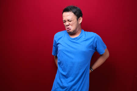Sad and upset young asian man with serious pain in back manの写真素材