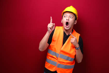 Shock Young asian man worker is surprised and shouting wow with pointing above with his hand isolated on red background.の写真素材