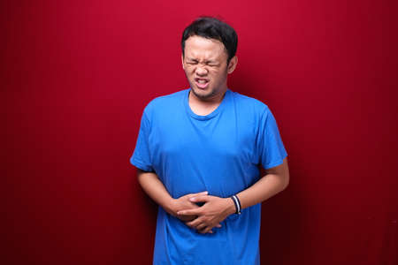 Upset young asian man with serious stomach acheの写真素材