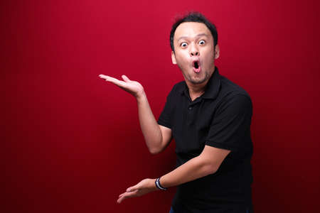 Young asian man is surprised and shouting wow with pointing right with his hand isolated on red background.の写真素材