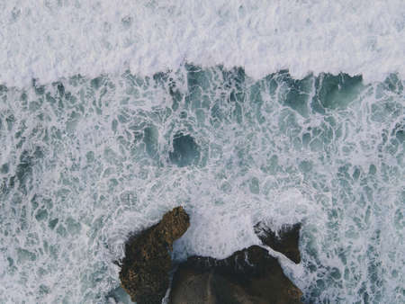 Top down aerial view of giant ocean waves crashing and foaming in coral beachの写真素材