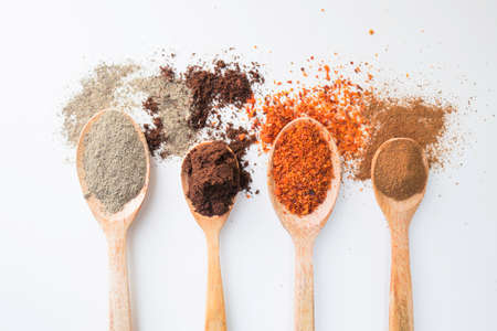Various spices on wooden spoons on white background