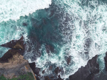 Top down aerial view of giant ocean waves crashing and foaming in coral beach