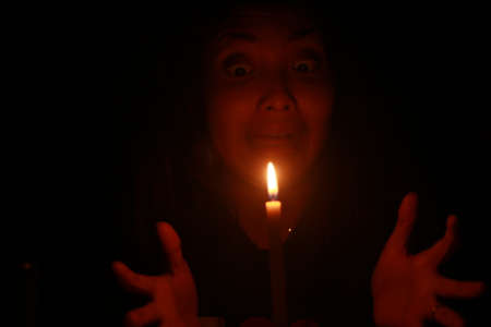 a spooky Asian woman shock with candle in the dark night