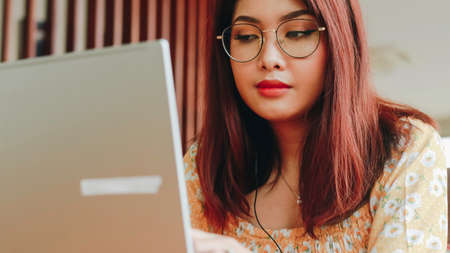 Young Asian woman working on laptop computer while sitting at the cafe, looking through documentsの写真素材