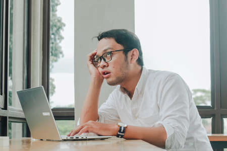 Depressed desperate businessman looking frustrated being overworked sitting at home office desk.の写真素材