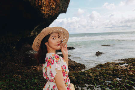 A young Asian girl wearing a beach hat is relaxing on the blue sky beach at Gunungkidul, Indonesiaの写真素材