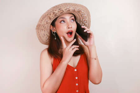 Shocked Asian woman wearing a straw hat talking on a mobile phone and laughing, expressing excitement emotions having a pleasant conversationの写真素材
