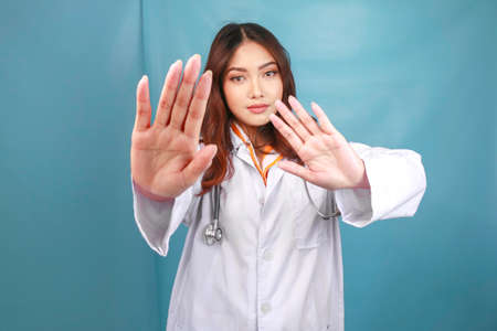Serious Asian female doctor with stethoscope and white coat, showing stop sign.の写真素材