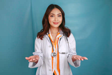 Young doctor woman presenting an idea while looking smiling on isolated blue backgroundの写真素材