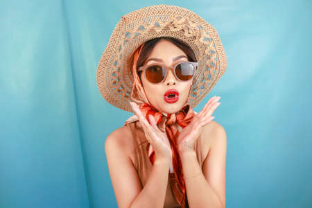 The traveling concept of a young Asian woman shocked and isolated by a blue background.