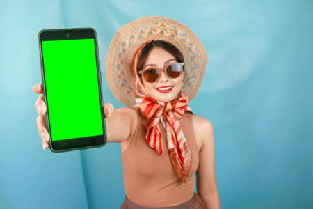 Traveling concept of a young Asian happy woman showing copy space on her smartphone isolated by a blue backgroundの写真素材