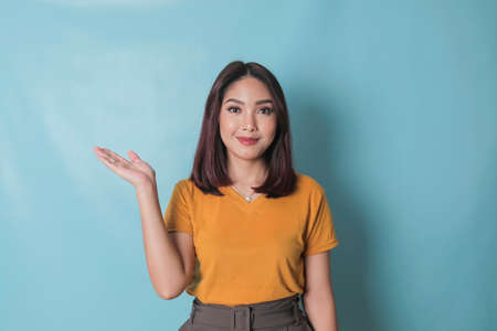 An excited young woman presenting and pointing upwards the copy space, isolated on blue backgroundの写真素材