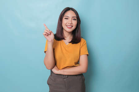 An excited young woman presenting and pointing upwards the copy space, isolated on blue backgroundの写真素材