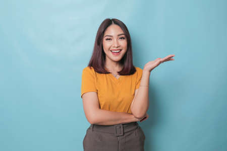 An excited young woman presenting and pointing copy space on her side, isolated on blue backgroundの写真素材