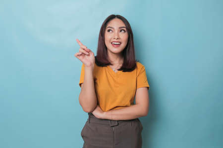 An excited young woman presenting and pointing upwards the copy space, isolated on blue backgroundの写真素材