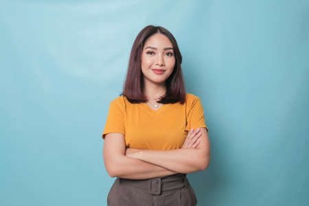 Portrait of a confident smiling girl standing with arms folded and looking at camera isolated over blue backgroundの写真素材