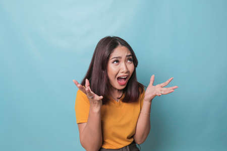 Beautiful young woman crying feeling very depressed isolated by blue background shouting loudの写真素材