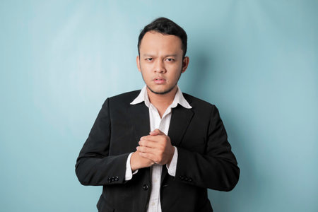 A portrait of a young Asian businessman looks angry and holding his fist ready to punch, isolated by blue backgroundの写真素材