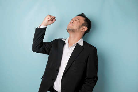 A young Asian man with a happy successful expression wearing suit isolated by blue backgroundの写真素材