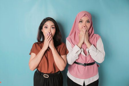 A portrait of two shocked Asian women gasping, isolated by a blue backgroundの写真素材