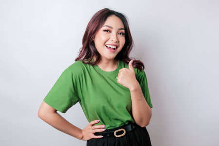 Excited Asian woman gives thumbs up hand gesture of approval, isolated by white backgroundの写真素材