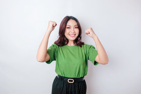 A young Asian woman with a happy successful expression wearing green shirt isolated by white backgroundの写真素材